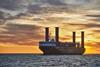 Wind-assisted cargo ship with four Flettner rotor sails at sea with a sunset behind