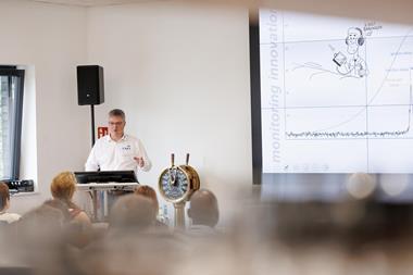A trainer stands by a white board and a ship's wheel training people