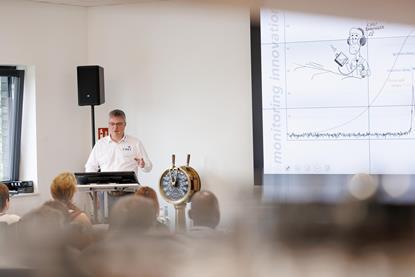 A trainer stands by a white board and a ship's wheel training people